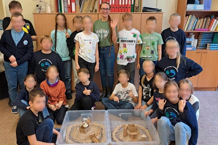 Klasėje, išpuoštoje popierinėmis girliandomis ir paveikslėliais, dirba vaikai su modelinu, jie lipdo pilį. Suolai išsidėstę aplink stalą ant kurio stovi kompiuteris su pavyzdžiu. Maži vaikai, užsidėję prijuostes, dirba kartu su mokytoja.