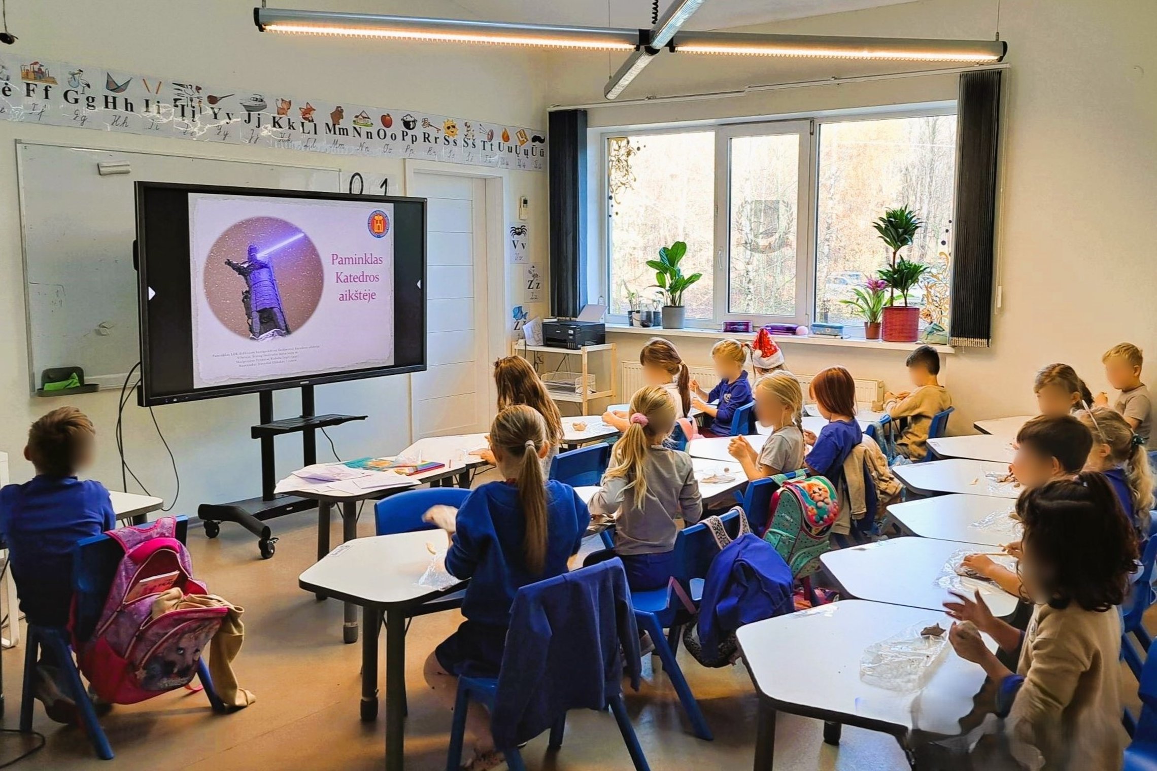 Nuoraukoje vaizduojami vaikai, sėdintys šviesioje klasėje. Dauguma dėvi mėlynus marškinėlius, kurie dera prie suolo kėdžių, kurios taip pat mėlynos. Vaikai užsiėmę lipdymu iš molio. Jie taip pat žiūri į projektoriuje rodomas skaidres.