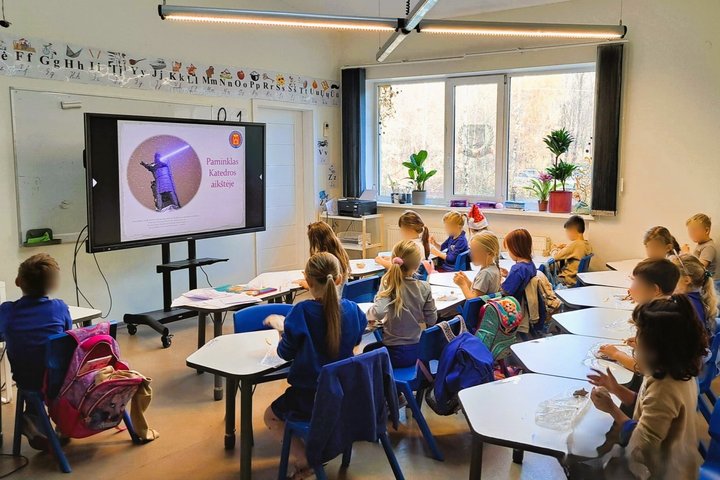 Nuoraukoje vaizduojami vaikai, sėdintys šviesioje klasėje. Dauguma dėvi mėlynus marškinėlius, kurie dera prie suolo kėdžių, kurios taip pat mėlynos. Vaikai užsiėmę lipdymu iš molio. Jie taip pat žiūri į projektoriuje rodomas skaidres.