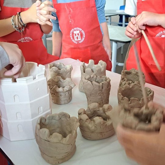 Nuotraukoje matome aštuonis vaikų iš molio nulipdytus Gedimino bokštus pastatytus ant stalo. Dar vienas nulipdytas bokštas yra vieno vaiko rankoje, jis ruošiasi pastatyti jį ant stalo. Šalia jų stovi pavyzdinė Gedimino bokšto figurėlė. Aplink stalą stovi 