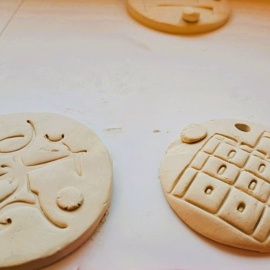 Dvi apvalios molio plokštelės su įspaustais ornamentais – viena vaizduoja stilizuotą pastatą su langais, kita – dekoratyvinius, vingiuotus simbolius. Abi dekoracijos turi skyles pakabinimui ir pritvirtintus mažus apskritimus. Jos padėtos ant balto pavirši