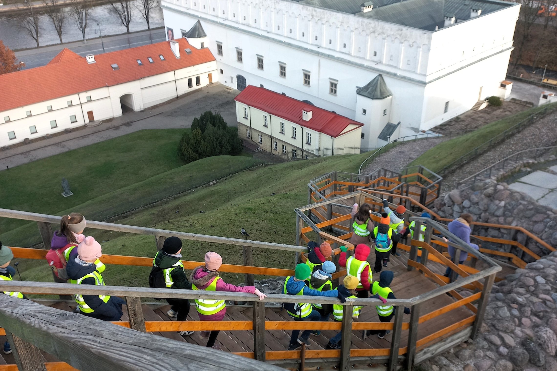 Nuotraukoje pavaizduota kaip darželinio amžiaus vaikai leidžiasi laiptais žemyn. Visuos juos jungiantis bruožas yra žalios ir itin ryškios atšvaitinės liemenės. Visi yra sustoję poromis po du ir juos veda moteris, dėvinti purpurinę pūkinę striukę.