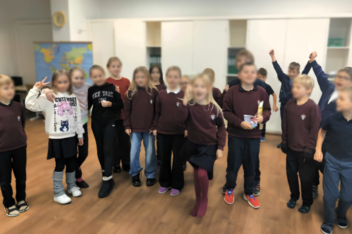 Nuotraukoje būrys nedidelių vaikų su mokyklinėmis uniformomis mokyklos klasėje. Už jų nugarų matosi lentynos su knygomis ir pasaulio žemėlapis. Vaikai atrodo linksmi, šypsosi. Kelios mergaitės kairėje pusėje apsikabinusios per pečius, o du berniukai nuotr