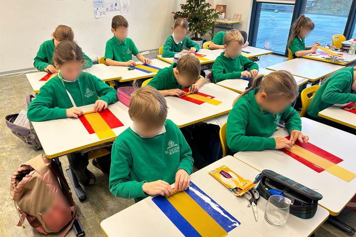 Nuotraukoje vaizduojami prie suolų sėdintys mokiniai. Visi mokiniai yra apsirengę žaliomis uniformomis. Klasės gale taip pat stovi Kalėdinė eglutė. Galima manyti, kad nuotrauka daryta šventiniu laikotarpiu.
