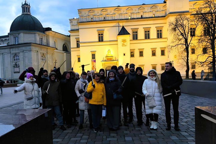 Nuotraukoje vaizduojama didelė žmonių grupė, kuri stovi prieš geltona šviesa apšviestus Lietuvos Didžiosios Kunigaikštystės valdovų rūmus vakaro tamsoje. Visi žmonės yra apsirengę šiltai su striukėmis, kepurėmis ir šalikais. Dauguma jų rankose laiko medin