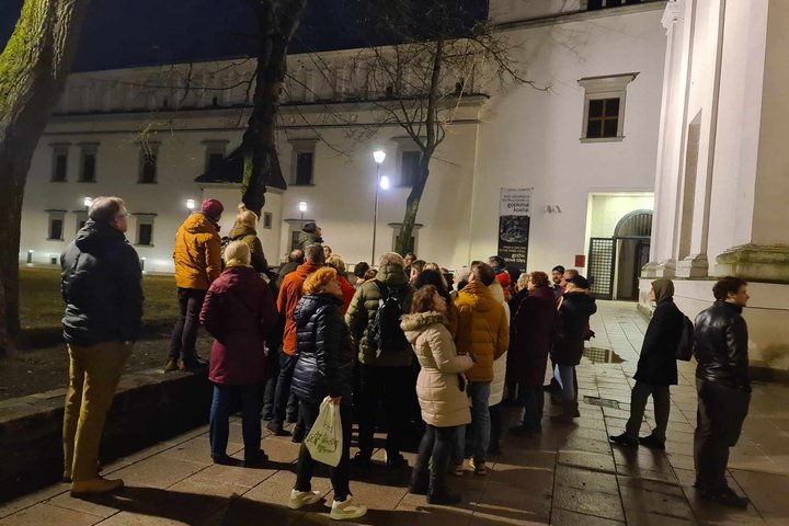 Grupė ekskursijos dalyvių Katedros aikštės šiaurinėje pusėje, aplink jau sutemę.