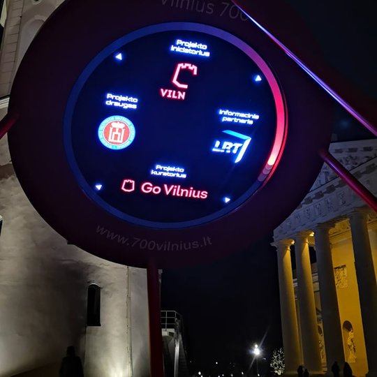 Pirmame plane šiek tiek kairiau yra raudona platforma ant kurios sumontuotas laikrodis, kuris skaičiuoja laiką, likusį iki septyni šimtojo Vilniaus miesto gimtadienio. Laikrodžio centre - logotipai draugų ir partnerių. Tarp kitų yra ir Vilniaus pilių reze