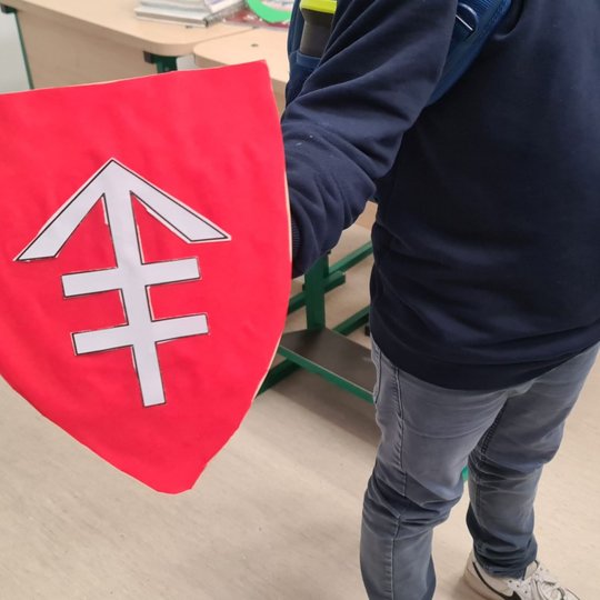 Berniukas rodo rankose laikomą raudoną herbą su Vytauto kryžiumi.