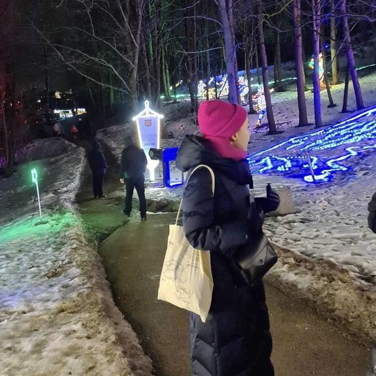 Matosi žmonės Kalnų parko take, kuris padengtas sniegu. Sniege švyti šviesų instaliacijos.