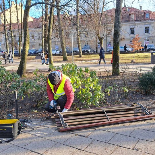 Meistras demontuoja seną, sulūžusį suolą Pilių parke, prie geriamojo vandens stotelės.