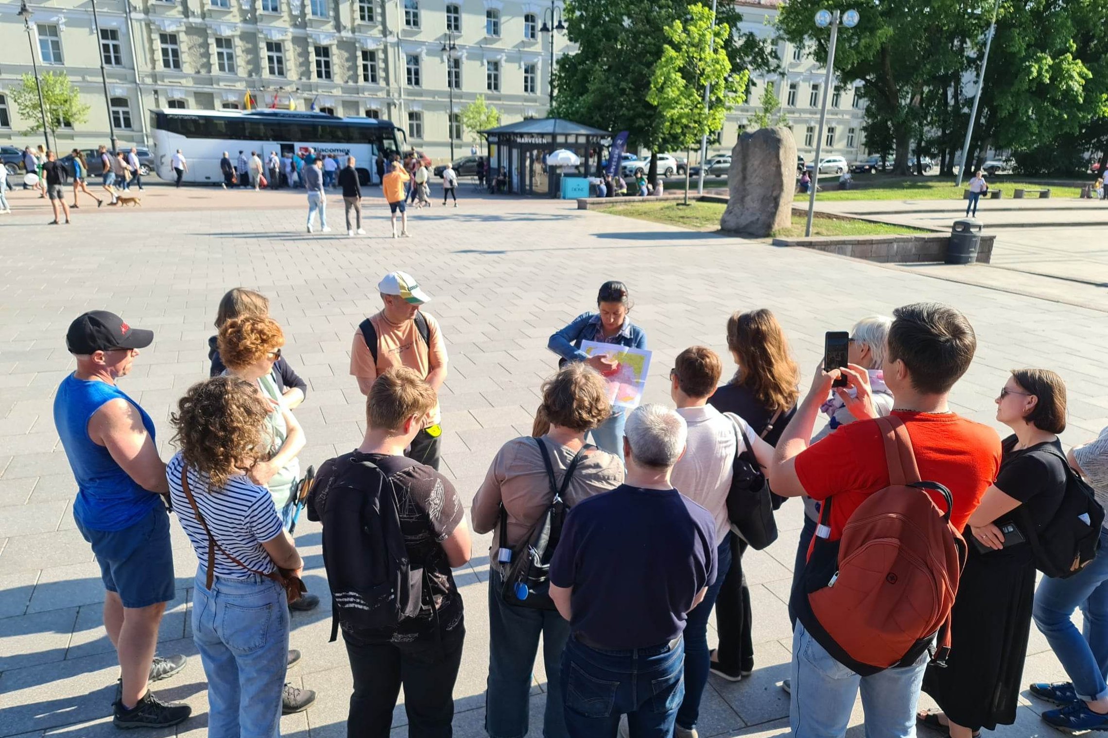 Ekskursijos dalyviai klausosi gidės pasakojimo apie Vilniaus pilis Katedros aikštėje, prie Gedimino paminklo.
