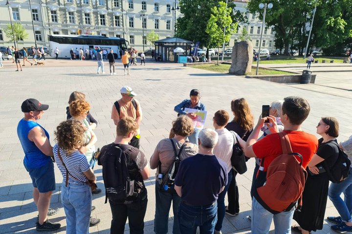 Ekskursijos dalyviai klausosi gidės pasakojimo apie Vilniaus pilis Katedros aikštėje, prie Gedimino paminklo.