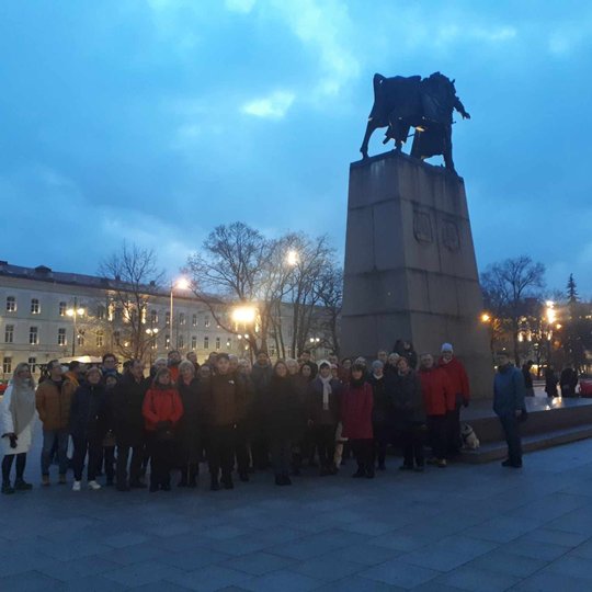 Ekskursantai, susibūrę prie Gedimino paminklo. Lauke jau temsta.