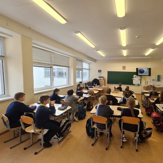 Nufotografuoti vaikai klasėje, sėdintys suoluose.