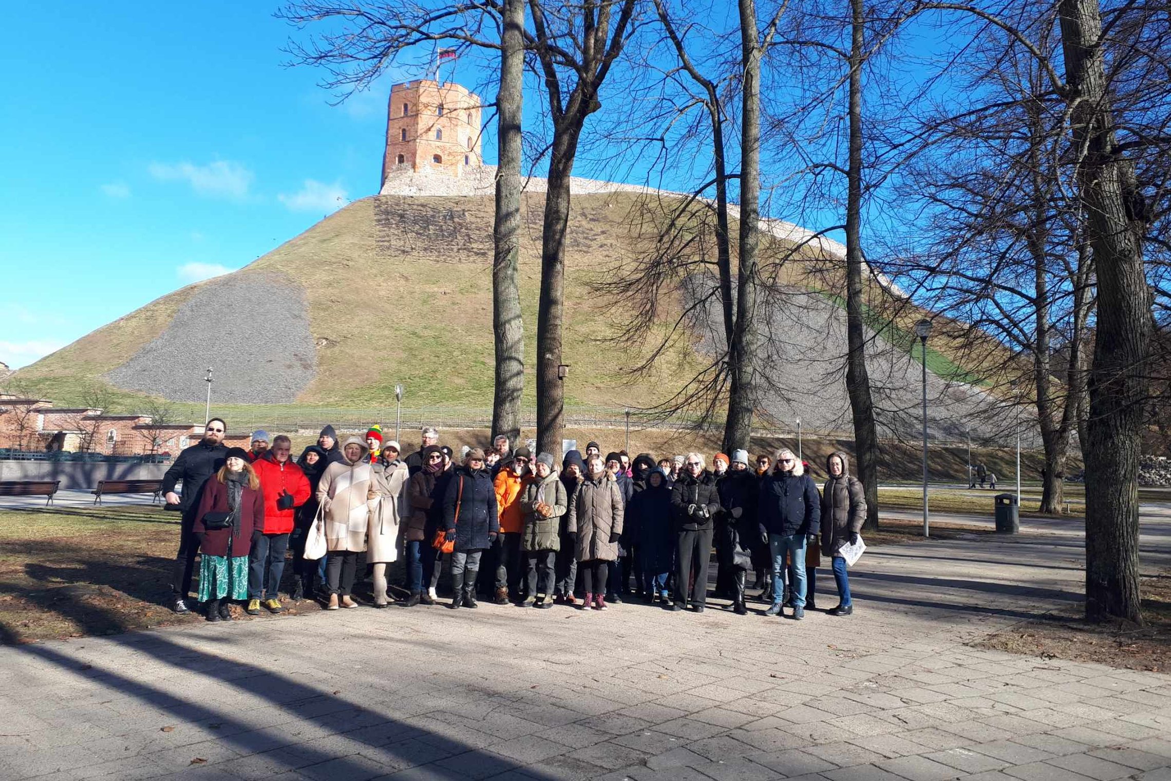 Grupė ekskursijos dalyvių Sereikiškių parke. Už jų matosi Gedimino pilies bokštas.