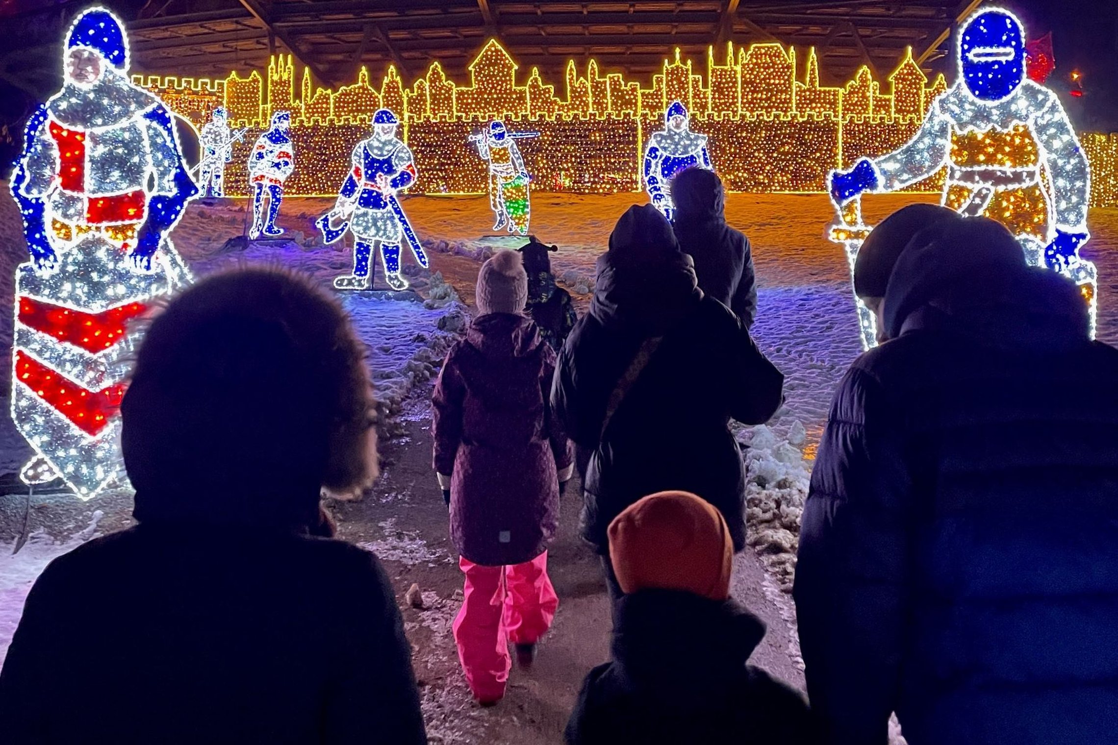 Tėvai ir vaikai eina šviesų instaliacijų link Kalnų parke.