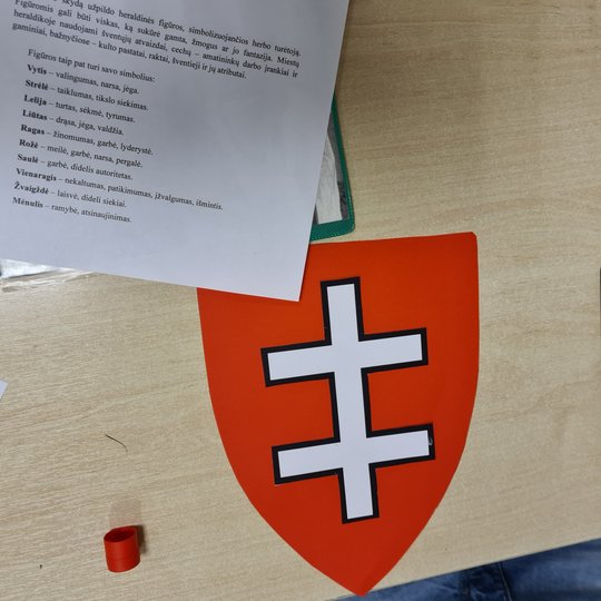 Ant klasės suolo paguldytas herbas. Šalia jo baltas lapas su herbo simbolių paaišikinimais.