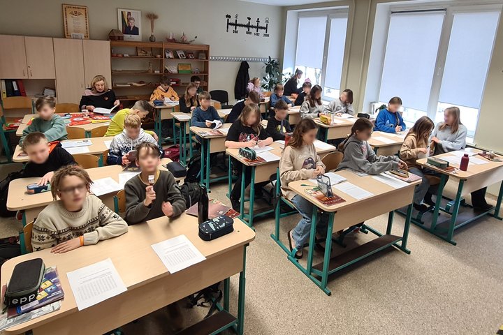 Penktokų klasė, sėdintys suoluose. Jie pozuoja kamerai.