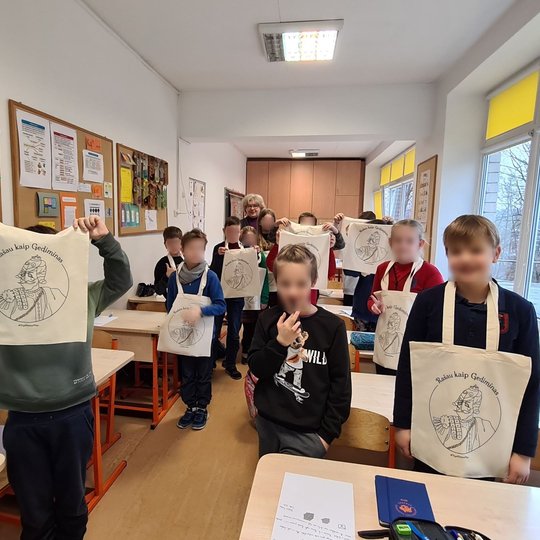 Vaikai stovi klasėje, rodo iškėlę medžiaginius Vilniaus pilių maišelius.