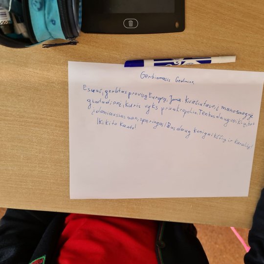 Berniuko laiškas Gediminui klasės suole. MAtosi berniuko ranka, laikanti rašiklį.