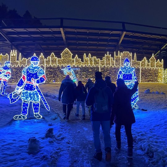 Vaikų grupė keliauja estrados link. Aplink juos yra pilies sargų instaliacijos.