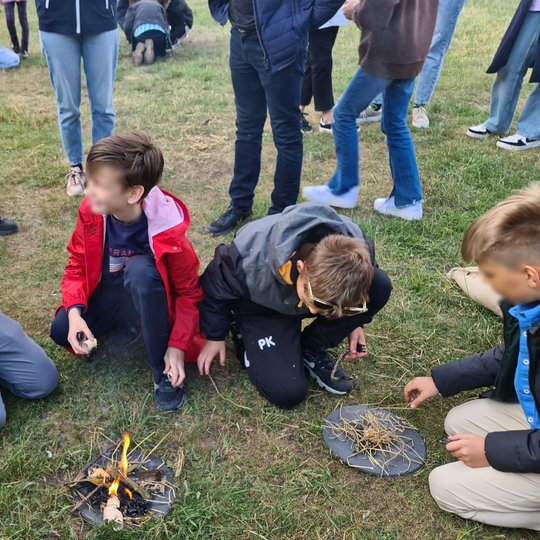 Mokinių grupelė džiaugiasi, sugebėję įkurti ugnį skiltuvais.