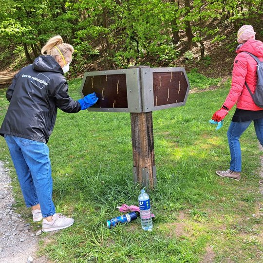 Dvi savanorės prie informacinės rodyklės ne tik valo, bet ir vandeniu plauna grafiti tagus.