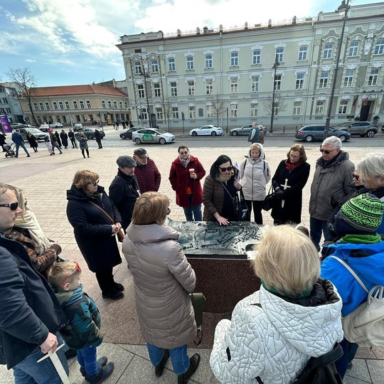 Ekskursijoje dalyvavę žmonės stovi aplink Vilniaus Žemutinės ir Aukštutinės pilių maketą, esantį Kudirkos aikštėje, ir klausosi pasakojimo.