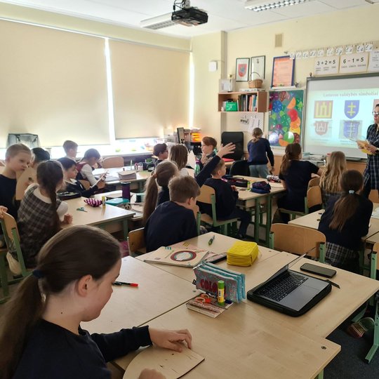 Mokiniams dėstoma edukacinė istorijos pamoka. Vienas iš mokinių klasėje kelia ranką.