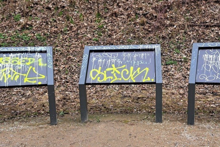 Trys informaciniai stendai, apipurkšti grafiti ir apipiešti markeriais Pilių parke prie Vilnelės upės.