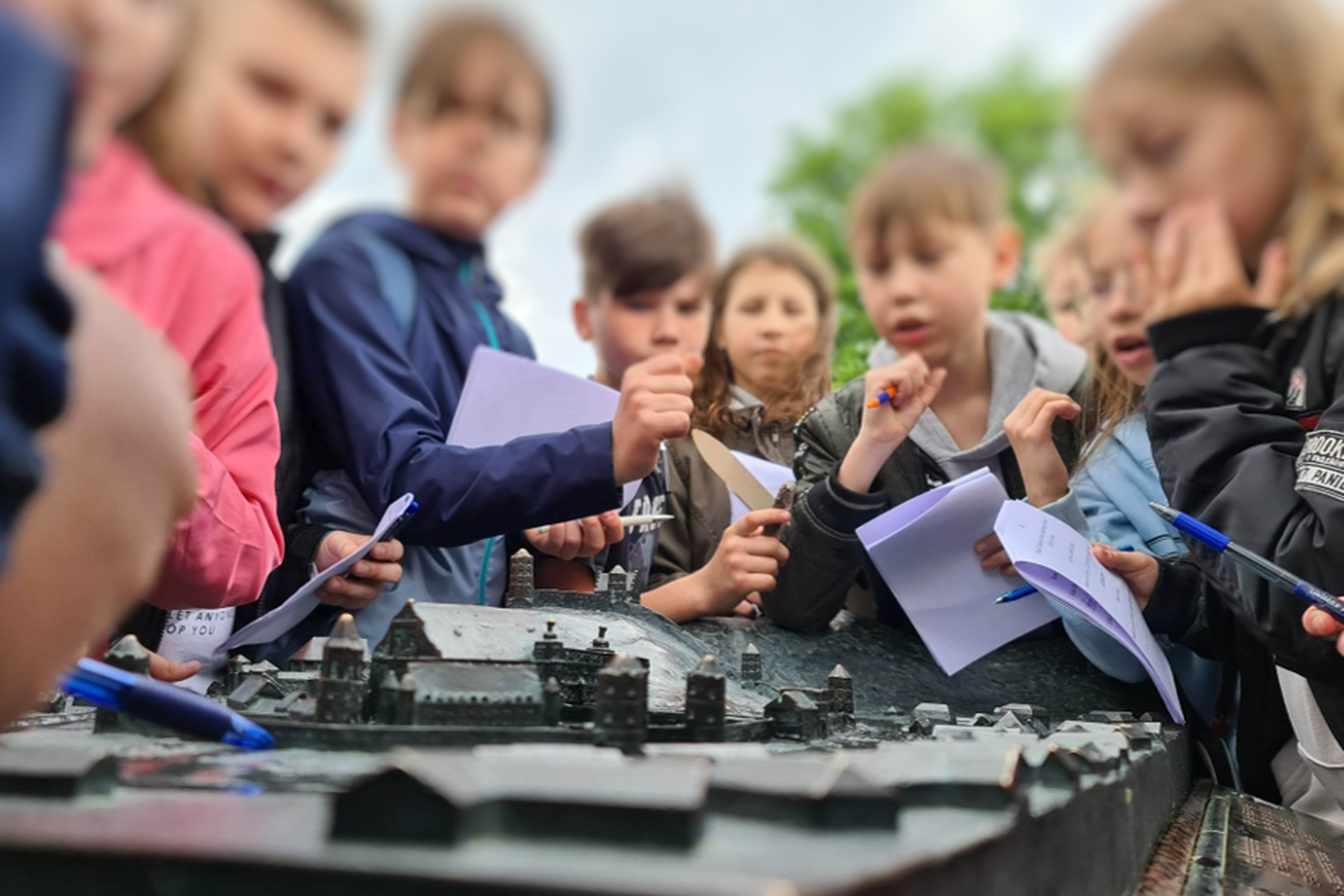 Vaikai su užduočių lapais, susirinkę prie Aukštutinės ir Žemutinės pilies maketo.