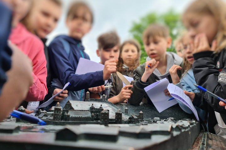 Vaikai su užduočių lapais, susirinkę prie Aukštutinės ir Žemutinės pilies maketo.
