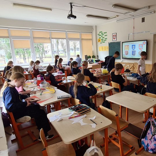 Kitoje klasėje taip pat vyksta kūrybos procesas, ant suolų karpomas popierius...