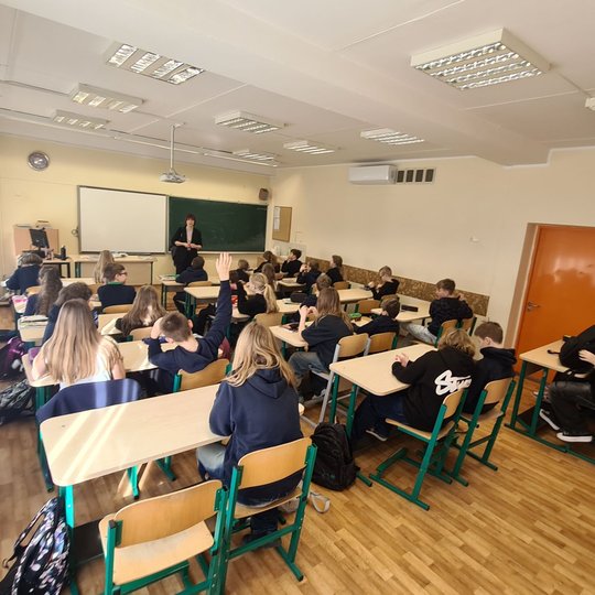 Penktokų klasė fotografuota iš klasės galo. Priekyje stovi mokytoja.