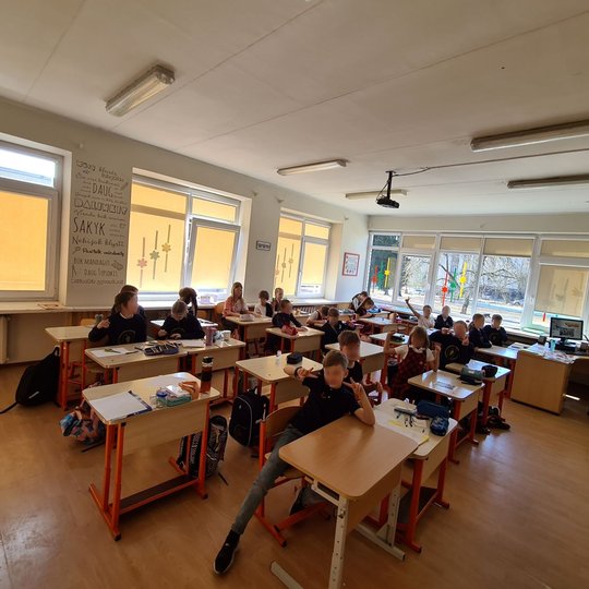 Mokiniai pozuoja klasės suoluose.
