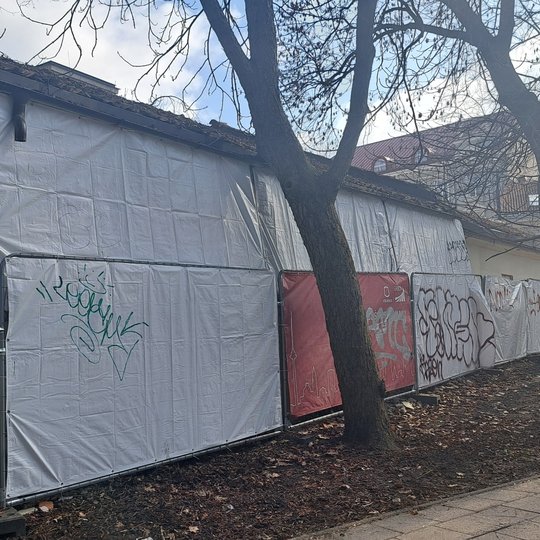 Nufotografuotos graffiti dažais išpieštos segmentinės tvoros prie vežiminės pastato.