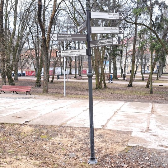 Nufotografuotas stulpas Sereikiškių parke, ant kurio įrengtos nukreipiamosios rodyklės. Jos visos tvarkingos.
