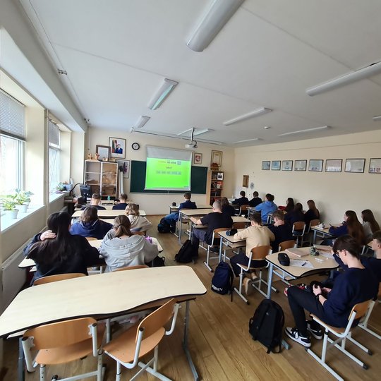 Aštuntokai sėdi klasės suoluose. Prieš juos projektoriuje matoma pamokos tema.