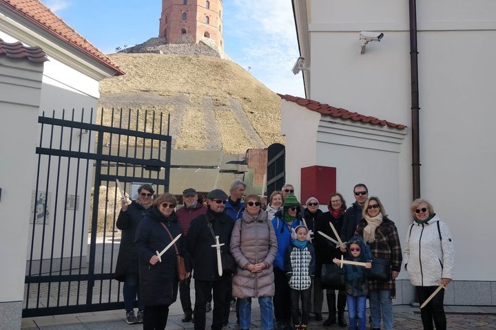 Sekmadienio ekskursijos dalyviai stovi prie Nacionalinio muziejaus ir Valdovų rūmų vartų. Už jų matosi Gedimino pilis.