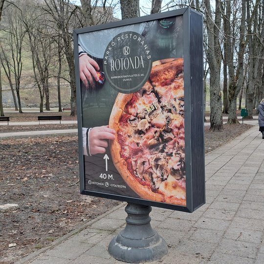Naujai įstatytas kavinės plakatas informaciniame stende. Jame vaizduojama pica ir „Rotondos“ kavinės kontaktai.