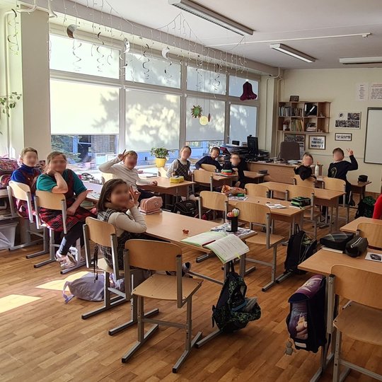 Mokiniai nufotografuoti, sėdintys klasės suoluose, iš klasės galo.
