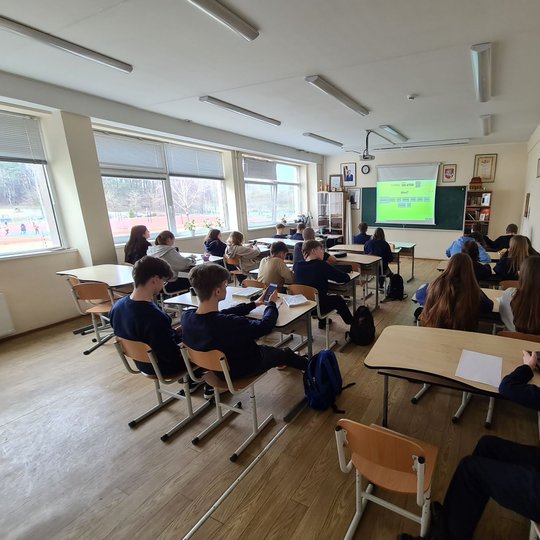 Aštuntokai sėdi klasės suoluose. Prieš juos projektoriuje matoma pamokos tema.