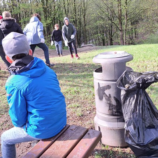 Mokiniai pailsėjimo stotelėje ant Stalo kalno. Vienas mokinys sėdi ant suolo, kiti išdykauja.