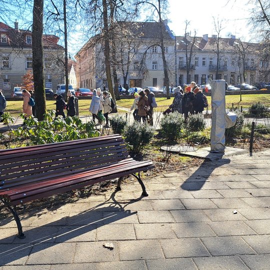 Restauruotas lauko suolas parke. už jo eina mokinukų ekskursija.