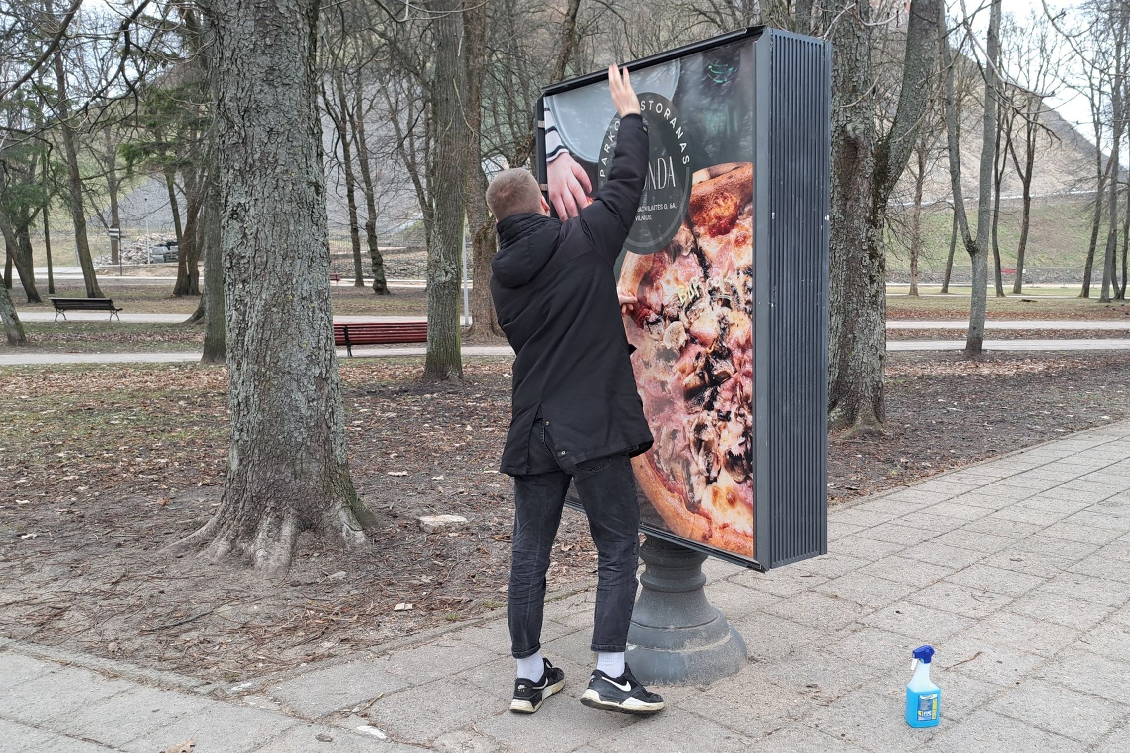 Kavinės darbuotojas tvirtina informacinio stendo kraštus.