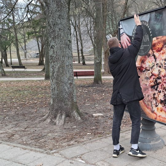 Kavinės darbuotojas tvirtina informacinio stendo kraštus.
