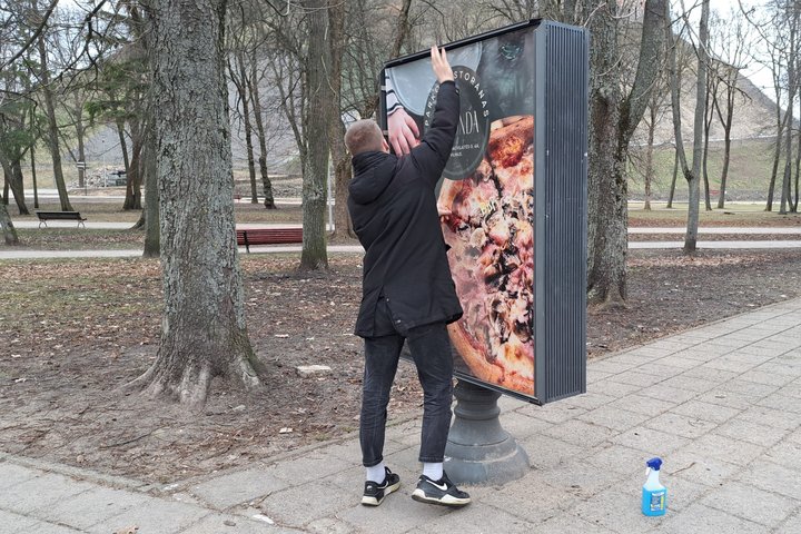 Kavinės darbuotojas tvirtina informacinio stendo kraštus.