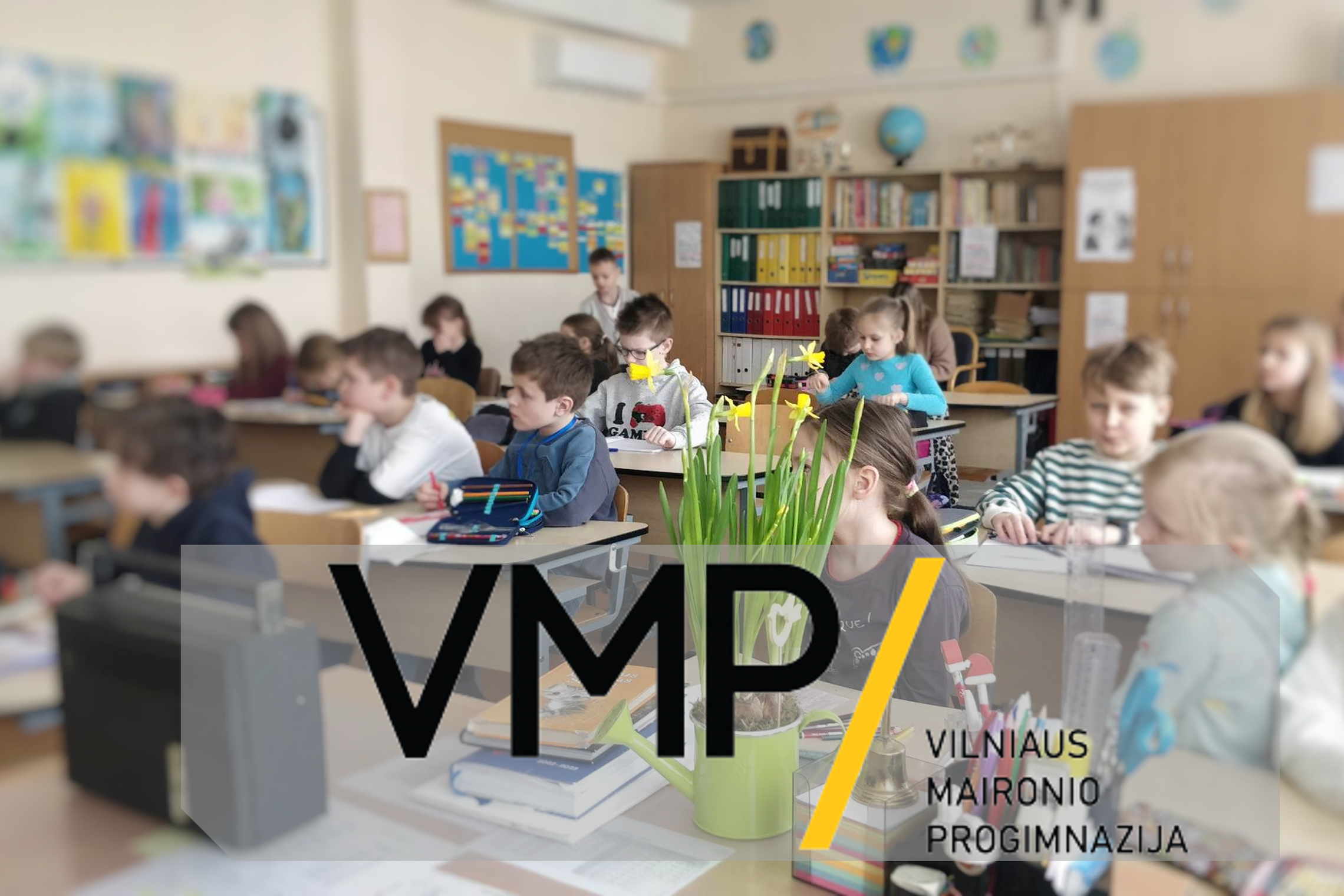 Nuotraukoje vaizduojamas Vilniaus Maironio progimnazijos ženklas (logotipas). Už jo - antrokai - sėdintys pamokoje.