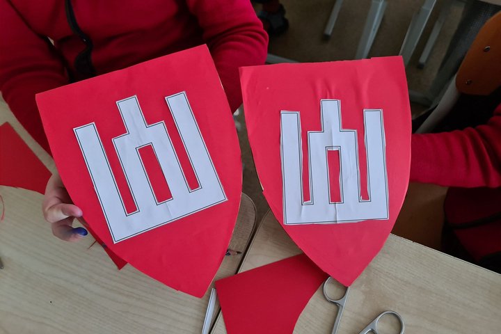 Nuotraukoje du raudoni vaikų pagaminti herbai, ant kurių puikuojasi balti Gediminaičių stulpai.