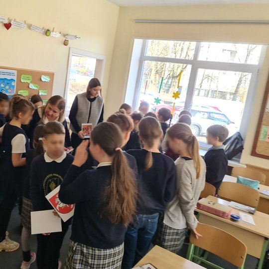 Vaikai, susibūrę klasės gale, rankose laiko lapus su herbais.